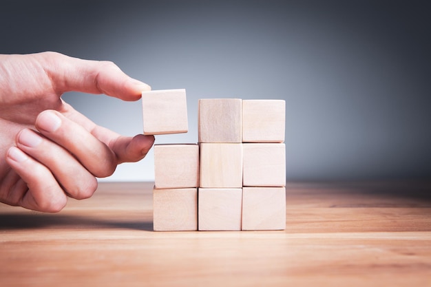 The man's hand adds a wooden block in place Business success concept