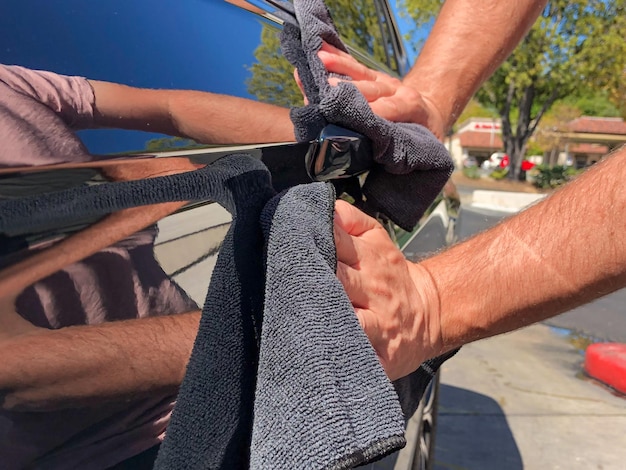 Man's hand cleaning the car with black microfiber cloth. Hand wipe down surface of car.