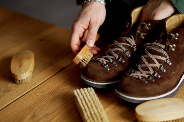 Photo man's hand cleaning suede shoes with a brush on wooden floor