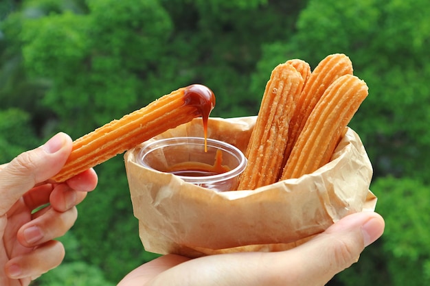 Man's Hand Dipping a Stick of Churro in Dolce de Leche Caramel Sauce