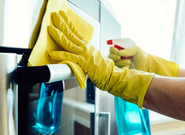 Man's hand in glove with rag cleaning oven