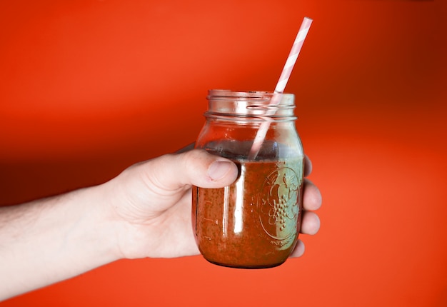 Man's hand holding a glass jar with berry smoothie on the white wall background.