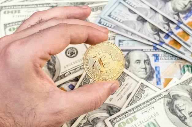 Man's hand holding golden bitcoin over background of US dollars