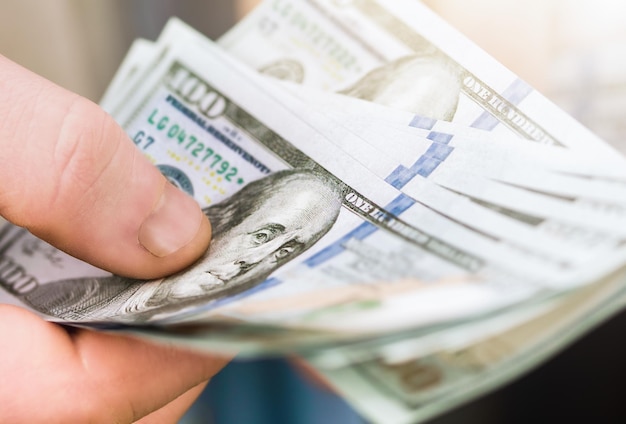 Man's hand holding hundred dollar bills