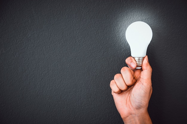 Man's hand holding LED light bulb  over black wall 