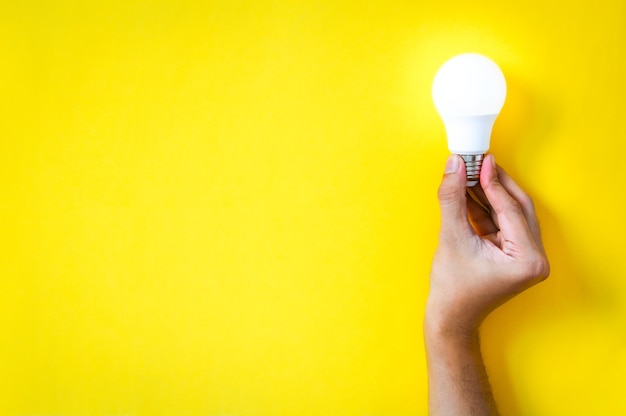 Man's hand holding LED light bulb over yellow color background, the concept of ideas