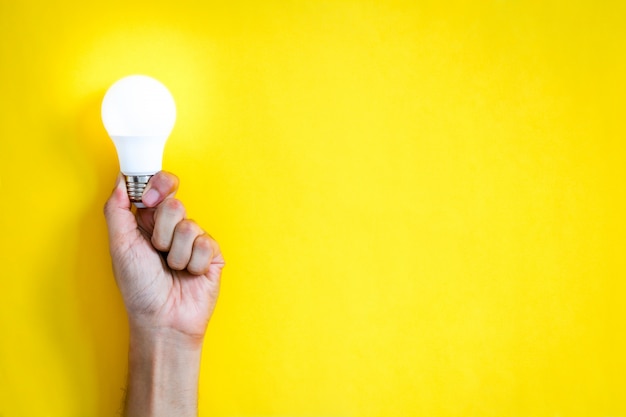 Man's hand holding LED light bulb over yellow color   