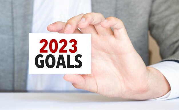 Man's hand holding paper card with 2023 goals words