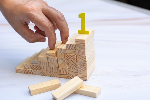 Man's hand holding a top of wooden blocks over wooden block