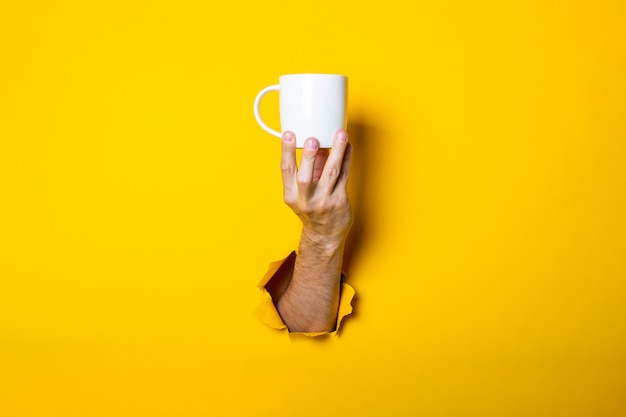 Man's hand holding a white cup on a bright yellow background