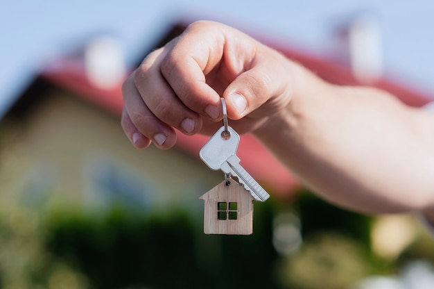 Man's hand holds the keys to the house against backdrop of residential buildings.