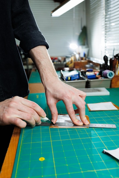 A man's hand holds pieces of leather for a leather wallet in his workshop The process of working with natural brown leather The craftsman holds the craft