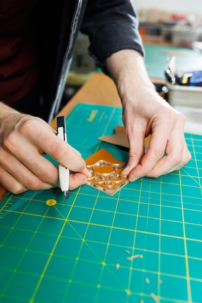 A man's hand holds pieces of leather for a leather wallet in his workshop The process of working with natural brown leather The craftsman holds the craft