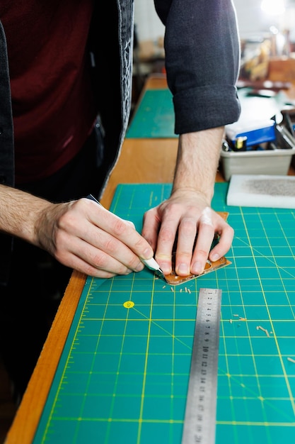 A man's hand holds pieces of leather for a leather wallet in his workshop The process of working with natural brown leather The craftsman holds the craft