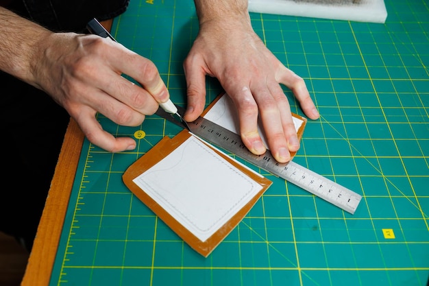 A man's hand holds pieces of leather for a leather wallet in his workshop The process of working with natural brown leather The craftsman holds the craft