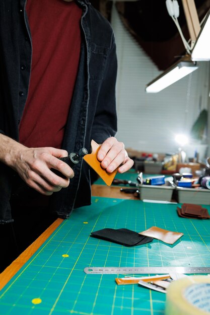 A man's hand holds pieces of leather for a leather wallet in his workshop The process of working with natural brown leather The craftsman holds the craft