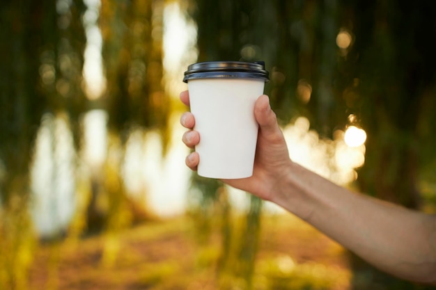 a man's hand holds a white cup of coffee on a blurred background. White glass. coffee.