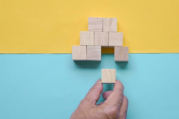 Man's hand inserting piece of wood block to complete a pyramid shape of wood blocks