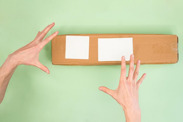 The man's hand is above a long paper box with white empty labels on a light green background Receiving parcel Happy Postal Service Ship Shipped Transit Transport Warehouse Address Carriage