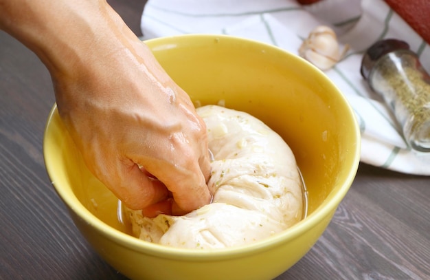 Man's hand kneading Italian bread dough mixed with garlic and herb in a mixing bowl