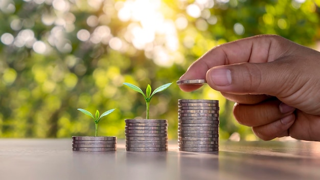 Man's hand placing silver coins on coins and trees growing on piles of coins finance business investment and growth concepts