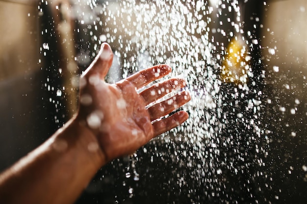 A man's hand in a spray of water in the sunlight against a dark background.