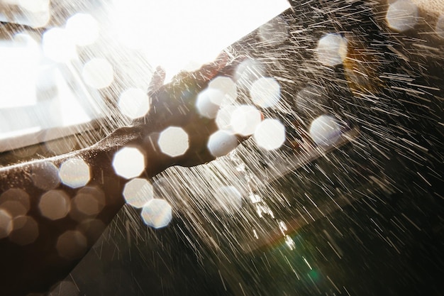 A man's hand in a spray of water in the sunlight against a dark background.