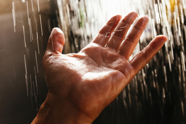 A man's hand in a spray of water in the sunlight against a dark background.