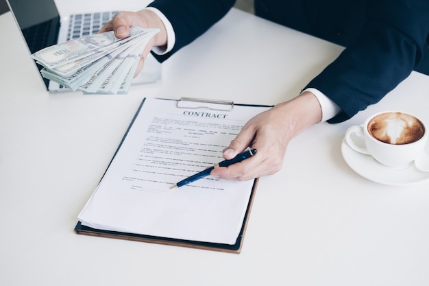 Man's hand in suit giving cash money and using pen point to signing