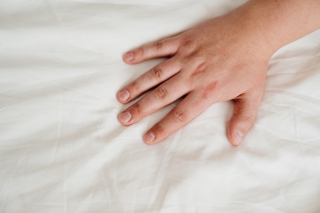 Man's hand on a white bed sheet.