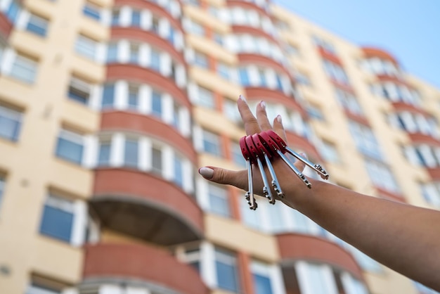 Man's hand with a key and a metal key chain house hanging from the side on the background of a fence and a cottage Construction project moving to a new home mortgage renting and buying real estate