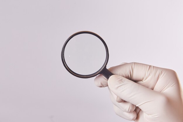 A man's hand with a latex glove uses a magnifying glass