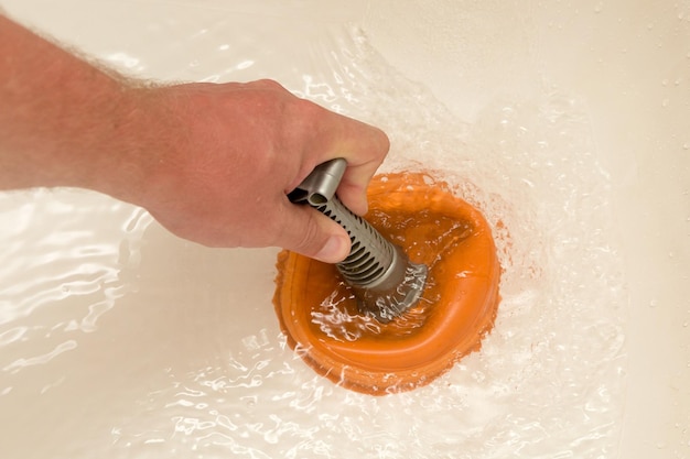 A man's hand with a plunger in the bath Cleaning pipes from blockages