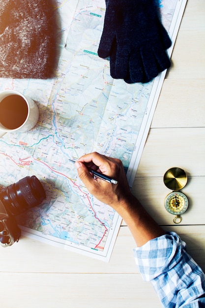 Photo man's hand writing on map with travel accessories on wooden table