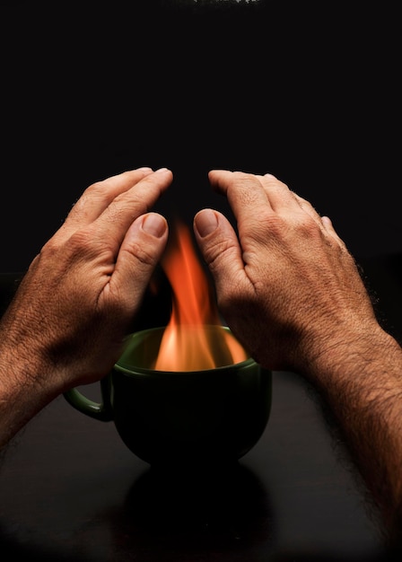 man's hands over cup with fire to warm up energy poverty