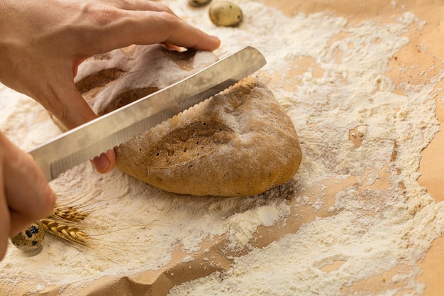 Man's hands cut a fresh wheat bun with a bread knife