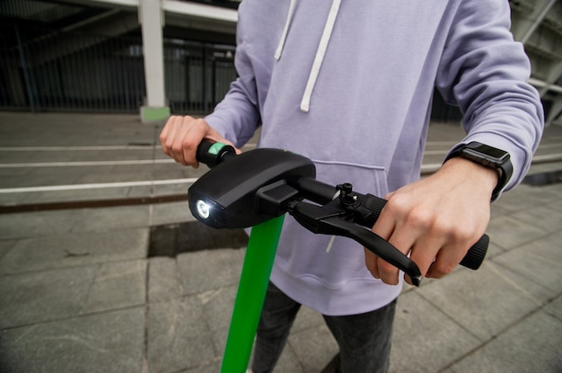 Man's hands hold steering wheel of electric scooter. Easy driving concept. Guy in casual gray hoody rented electric vehicle to travel around city. Eco-friendly transport concept.