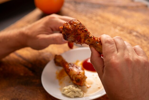 Photo man's hands holding chicken leg at the table