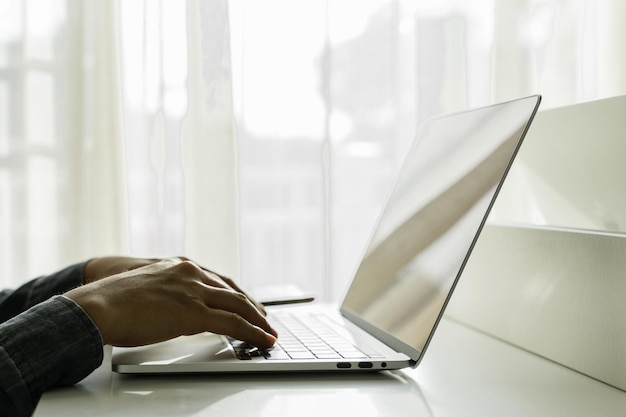 Man's hands using laptop computer with smartphone on white table at home Online shopping home work freelance online learning concept