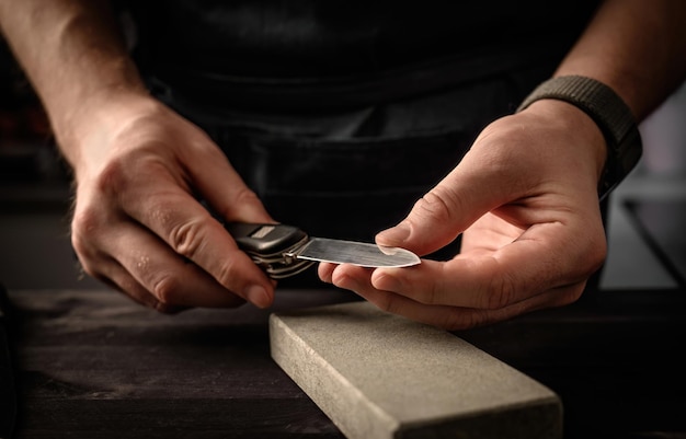 Man's hands with folding knife and sharpen stone tool master sharpening penknife on a grindstone