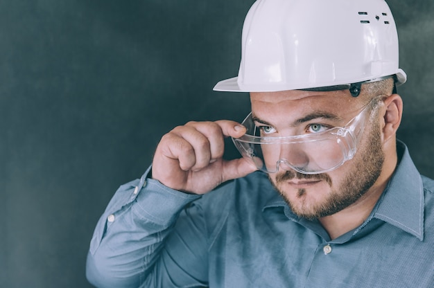 A man in safety glasses and a construction helmet on a dark background