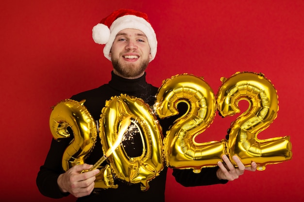 A man in a Santa Claus hat holds the numbers 2022 and a sparkler