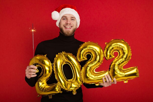 A man in a Santa Claus hat holds the numbers 2022 and a sparkler