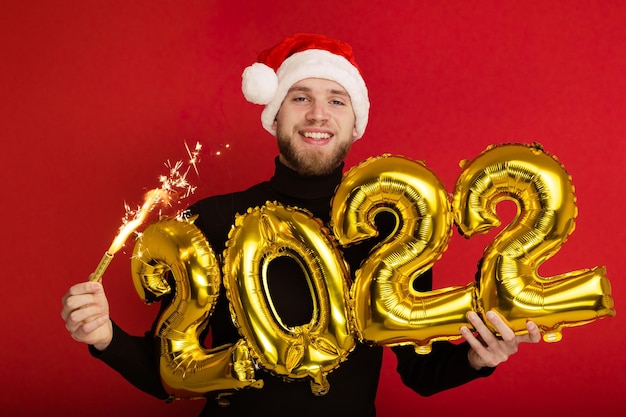 A man in a Santa Claus hat holds the numbers 2022 and a sparkler