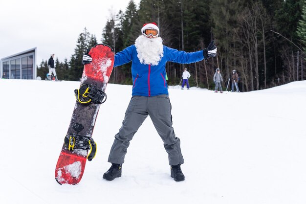 Man in Santa Claus hat with a snowboard at a ski resort.