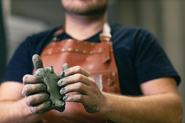 Photo man sculptor dressed leather apron with clay in hands statue craft creation workshop