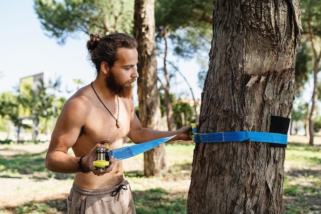 Man setting up slacklining equipment in city park during summer day