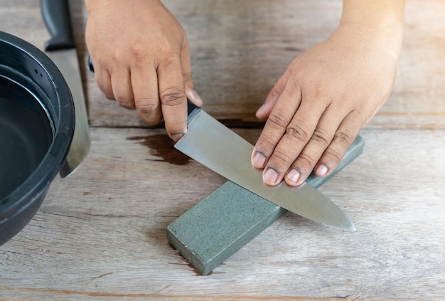 Photo the man sharpen kitchen knife with whetstone on wooden table