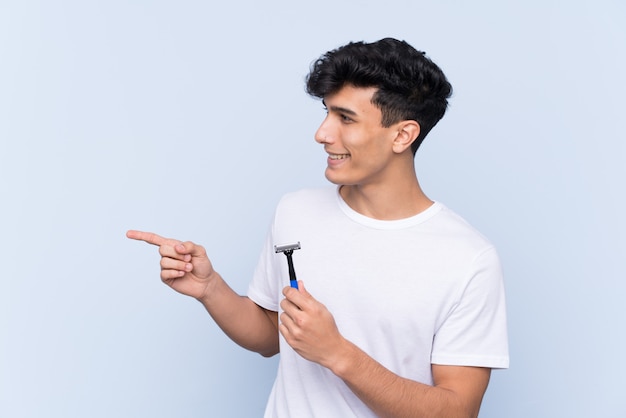 Man shaving his beard over isolated white wall pointing to the side to present a product