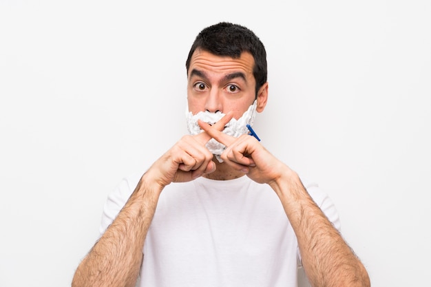 Man shaving his beard over isolated white wall showing a sign of silence gesture